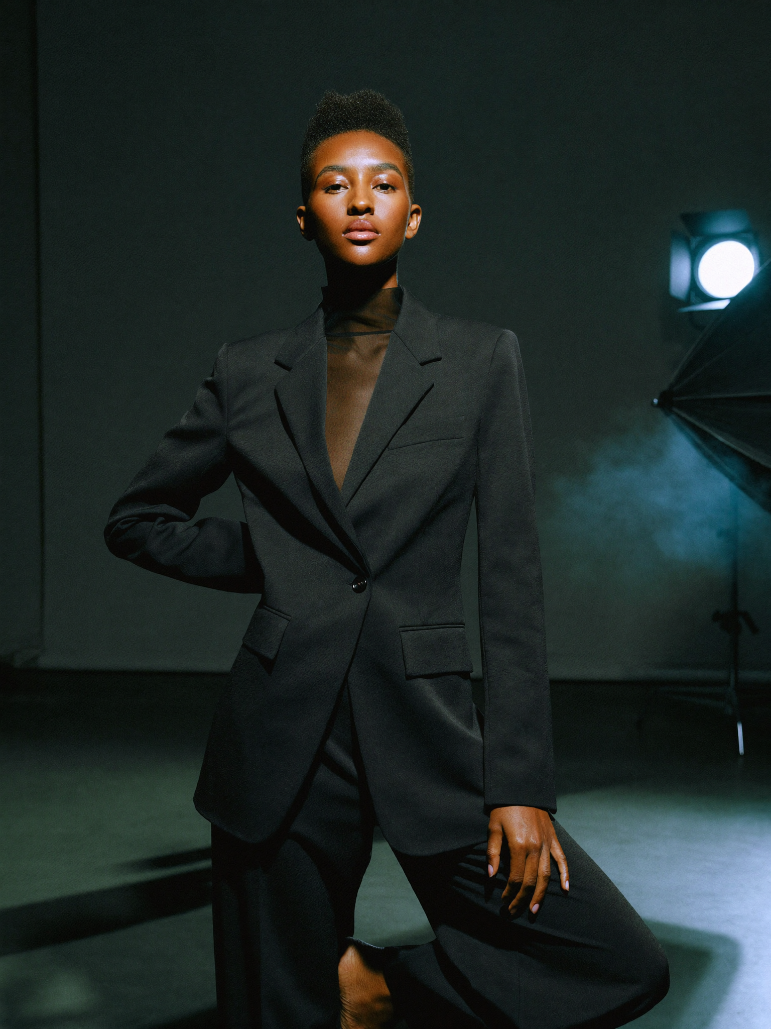 Model in matte black tailored suit, dark studio with key light.